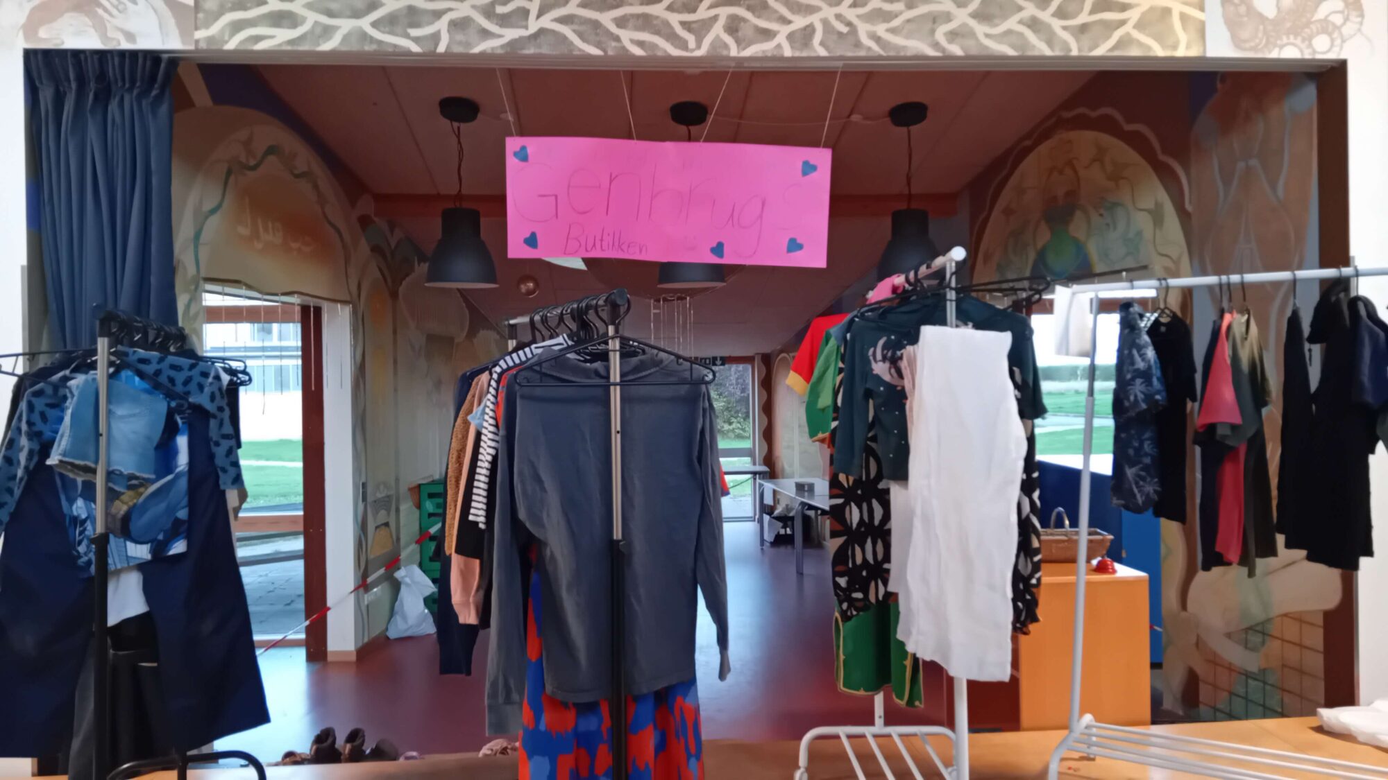 Genbrugsbutikken med tøjstativer og et lyserødt skilt med påskriften Genbrug Butikken.